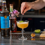 Cocktail being prepared with a bottle of Liber & Co Demerara Syrup in the background.