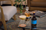 Cocktail glass with foam and bottle of Liber & Co Syrup on a table with blurred background