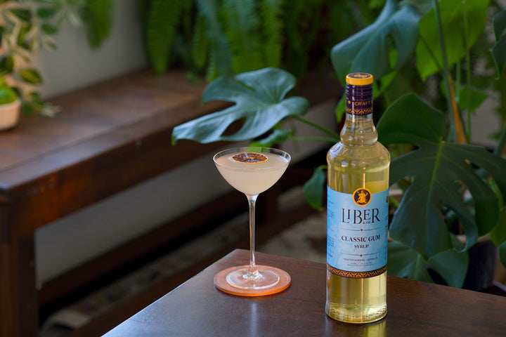 Bottle of Liber & Co. Classic Gin with a cocktail on a wooden surface with plants in the background