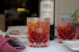 Two glasses of red cocktails with a bottle of Cocchi in the background on a table.