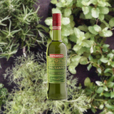 Green bottle of Luxardo Del Santo liqueur with a red cap against a green leafy background