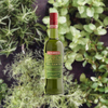 Green bottle of Luxardo Del Santo liqueur with a red cap against a green leafy background