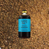 A large bottle of dark syrup with a canary blue label that reads: Liber & Co Demerara Gum Syrup.  This is set against a backdrop of pure raw sugar, dark and delicious.