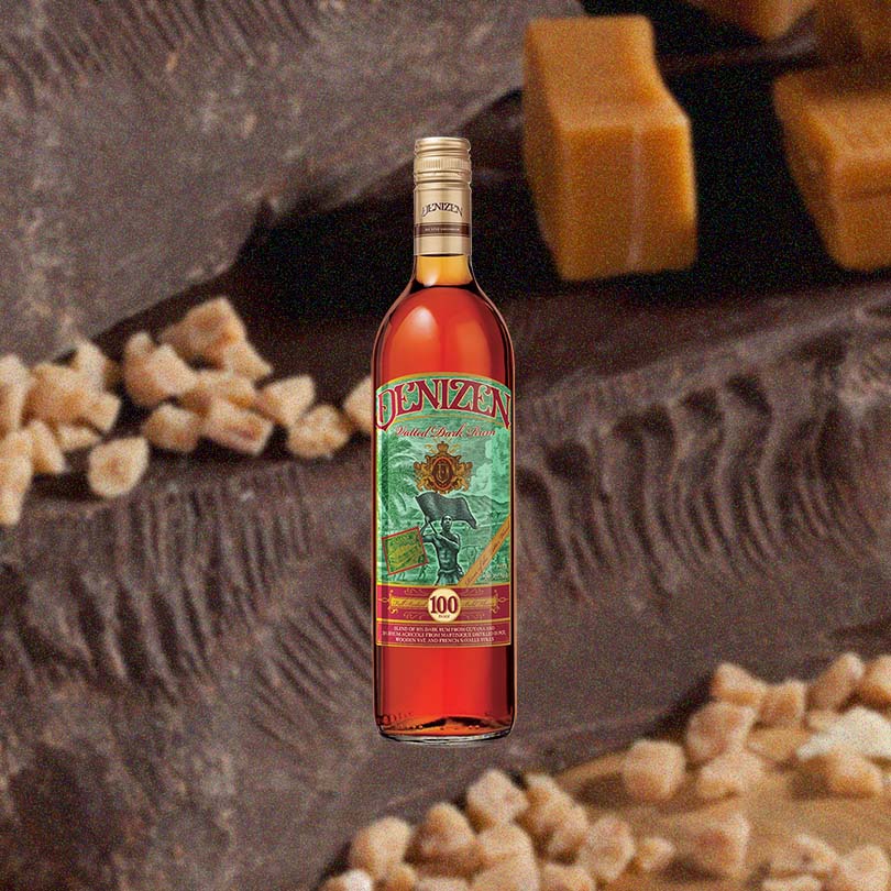 Bottle of Denizen Vatted Dark Rum over back drop image of chocolate, nuts, and caramels.