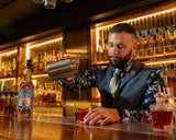 Bartender preparing a drink behind a bar with shelves of bottles in the background