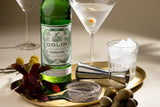 Dolin vermouth bottle with a cocktail glass, ice cubes, and olives on a tray.