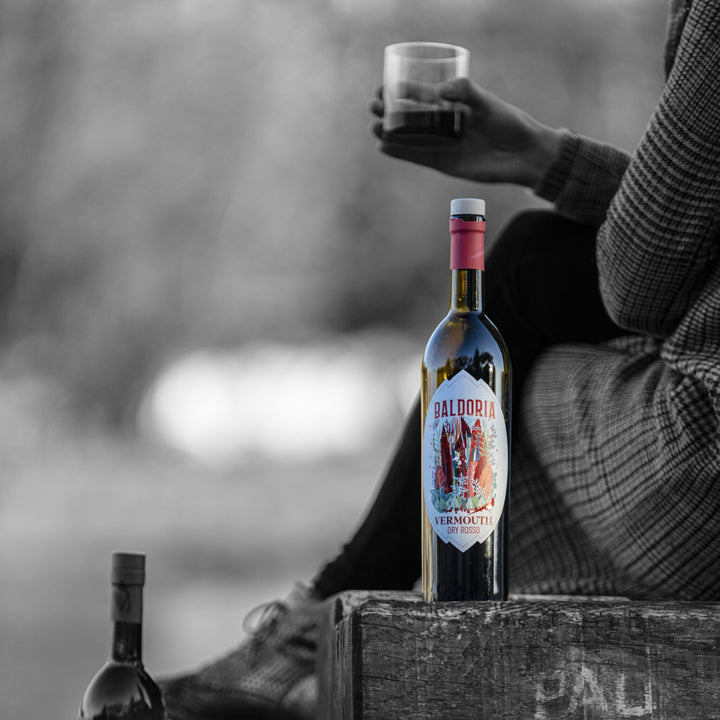 Bottle of Balderin Vermouth with a person holding a glass against a blurred background
