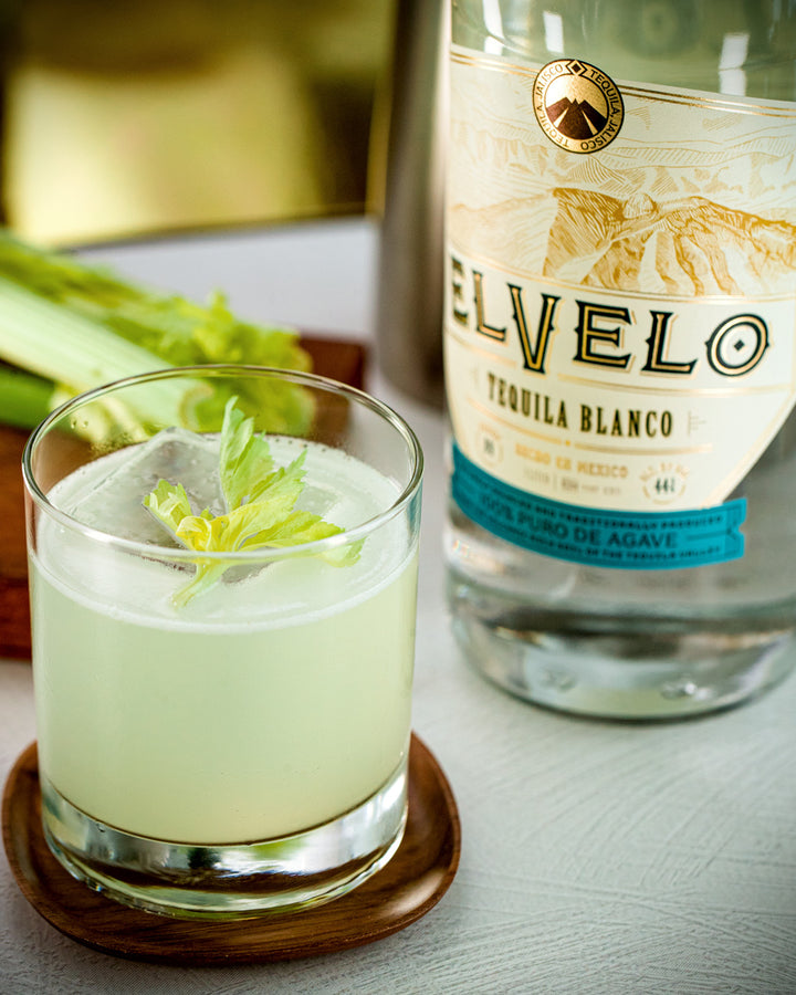 Glass of green cocktail with Elvelo tequila bottle in the background