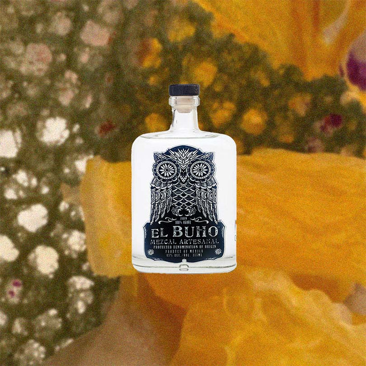 Bottle of El Buho Mezcal Artesanal Espadin over backdrop image of dried fruit up close.