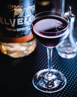 Glass of red wine with a bottle labeled 'El Vello' on a dark textured surface