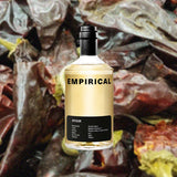 A refined looking minimalistic yellow bottle with the word EMPIRICAL on top in large black sans serif font. Ayuuk is on a black label at the bottom, including a list of ingredients: Botanicals - Pasilla Mixe; Yeast - Belgian Saison 2; Grains - Pilsner Malt, Purple Wheat. Against a backdrop of Pasilla Mixe chiles.