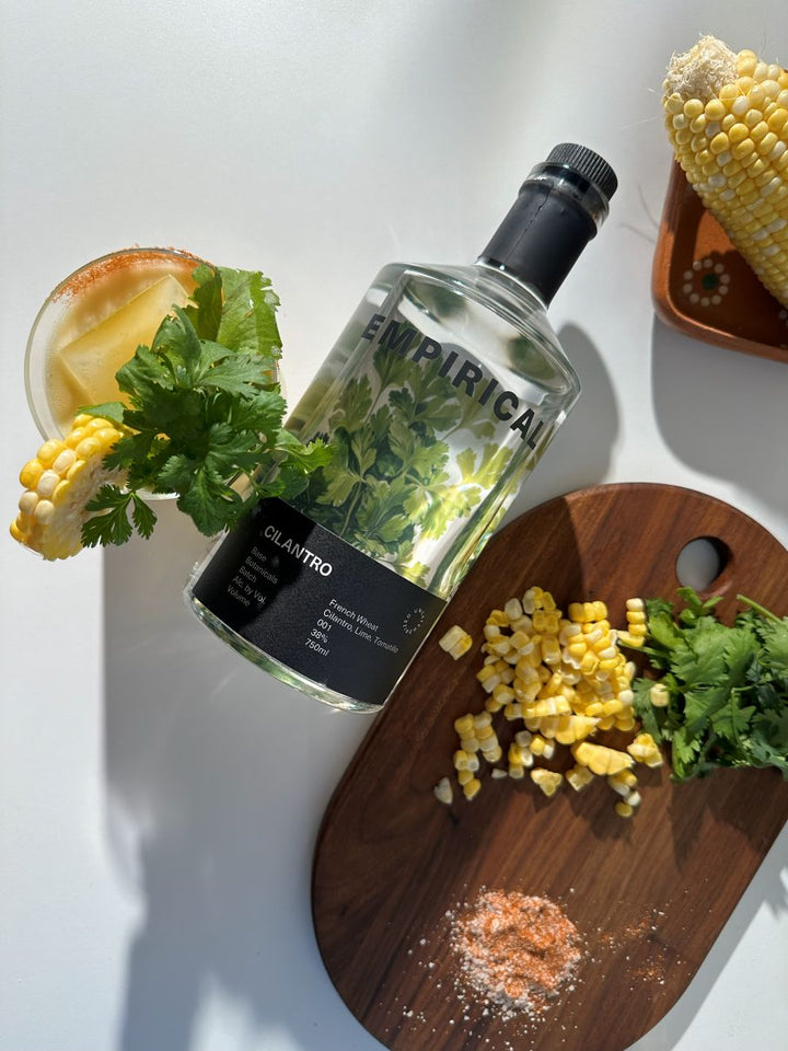 Bottle of Empirica cilantro-flavored vodka on a cutting board with corn and herbs.
