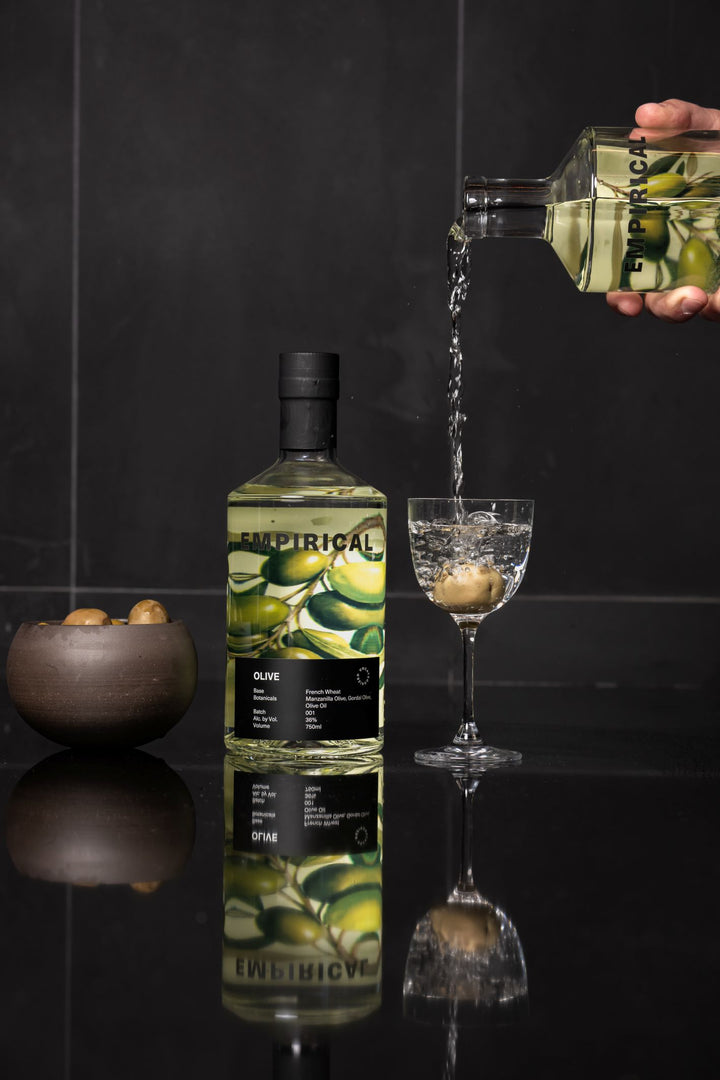 Bottle of Empirical Olive gin being poured into a glass with a dark background