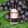 A bottle of Empirical Symphony 6 set against a macro shot of black current berries on a bed of bright grass.