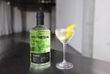 Bottle of Empirical Olancro gin with a cocktail garnished with a lemon twist on a dark surface.