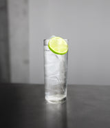 Clear glass with a lime wedge on a dark surface and gray background