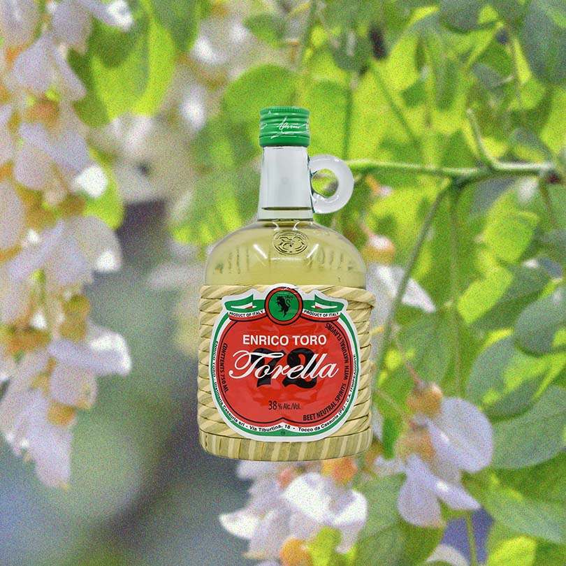 Bottle of Enrico Toro Torella 72 Digestif over backdrop of green leaves and white flowers.