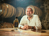 Man sitting at a wood table in a distillery with a bottle of The Lost Explorer Reposado Tequila on the table.