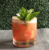 Cocktail in a glass with pineapple pattern and mint leaves against a green textured background