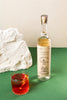 The tall bottle of Pierde Almas Mezcal to the right and a cocktail glass with a red liquid and a blood orange slice in it. All on a green and white backdrop.