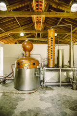 Alcohol distillery with copper stills and metal tanks in a warehouse setting.