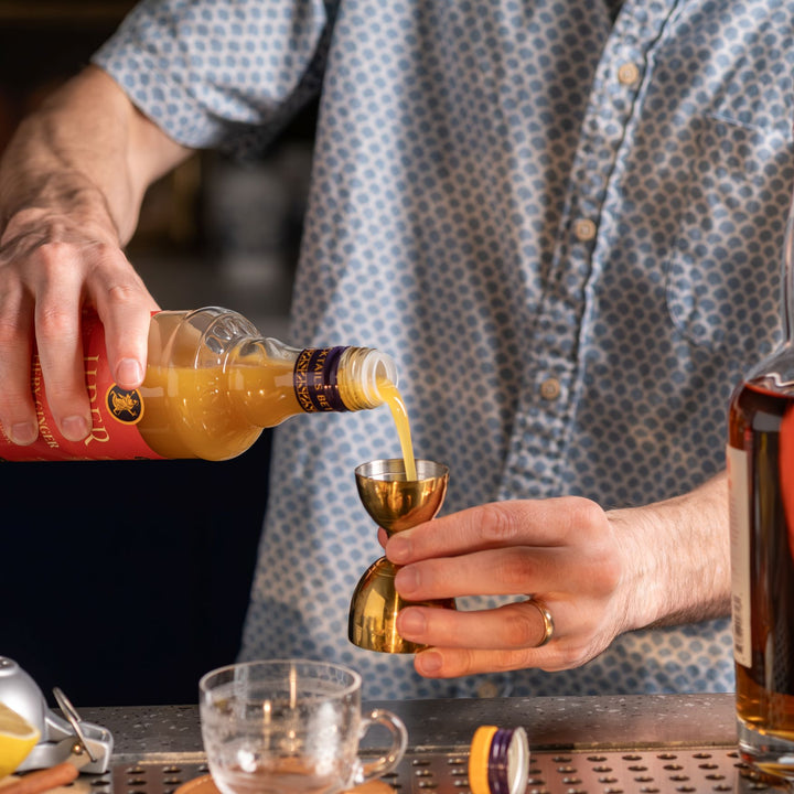 Person pouring a liquid from a bottle into a small gold cup with a blurred background