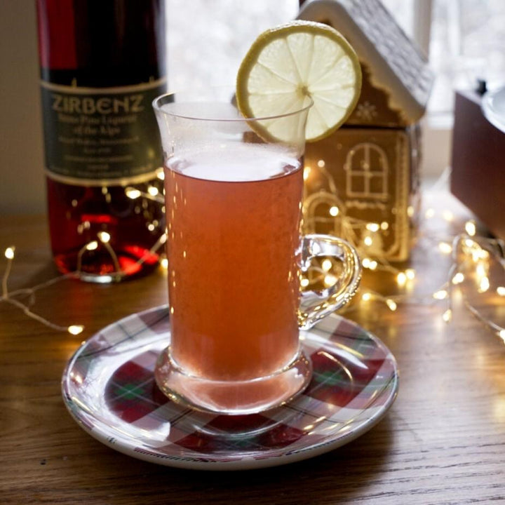 Glass of pink drink with a lime wedge on a checkered coaster, bottle in the background