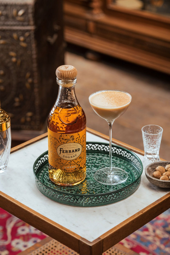 Bottle of Ferrand cognac on a green tray with a cocktail glass and other items on a table.