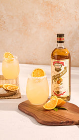 Bottle of Ferrand Dry Curacao with two glasses of lemonade on a wooden board.
