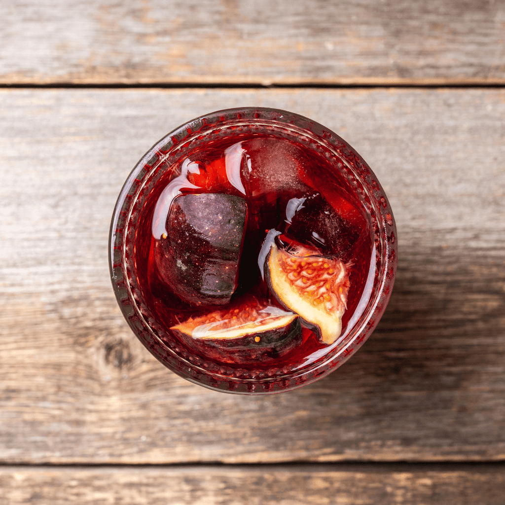 View looking down into a red cocktail over ice on a wood table.