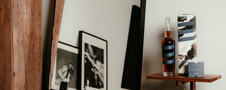 Bottle of whiskey on a wooden shelf with framed pictures and a card in the background.