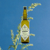 Bottle of Dolin Génépy le Chamois Liqueur over backdrop image of a blue sky and green flower.