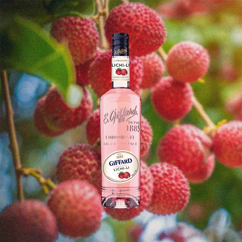 Bottle of Giffard Lichi-Li Liqueur over backdrop image of fruit, plants.
