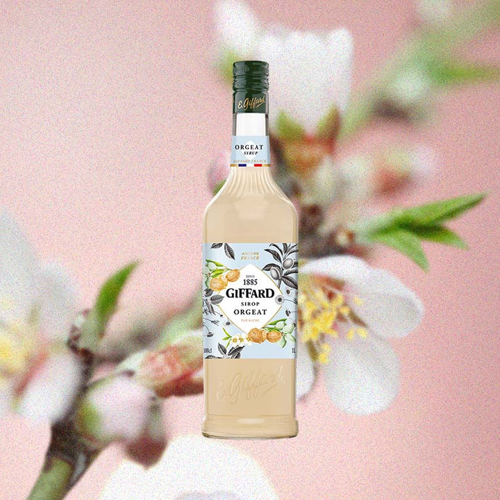 Bottle of Giffard Orgeat Syrup over backdrop of a flower.