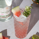 Cocktail with watermelon and cucumber garnish next to a bottle of Gin Lane gin.