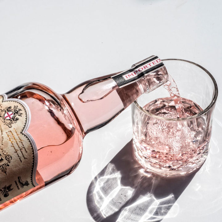 Rose wine being poured from a bottle into a glass on a light background