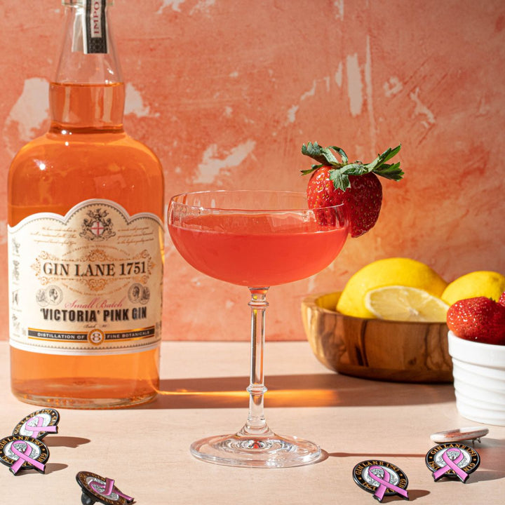 Bottle of Gin Lane 1751 Victoria Pink Gin with a cocktail garnished with strawberries and lemons on a textured pink background.