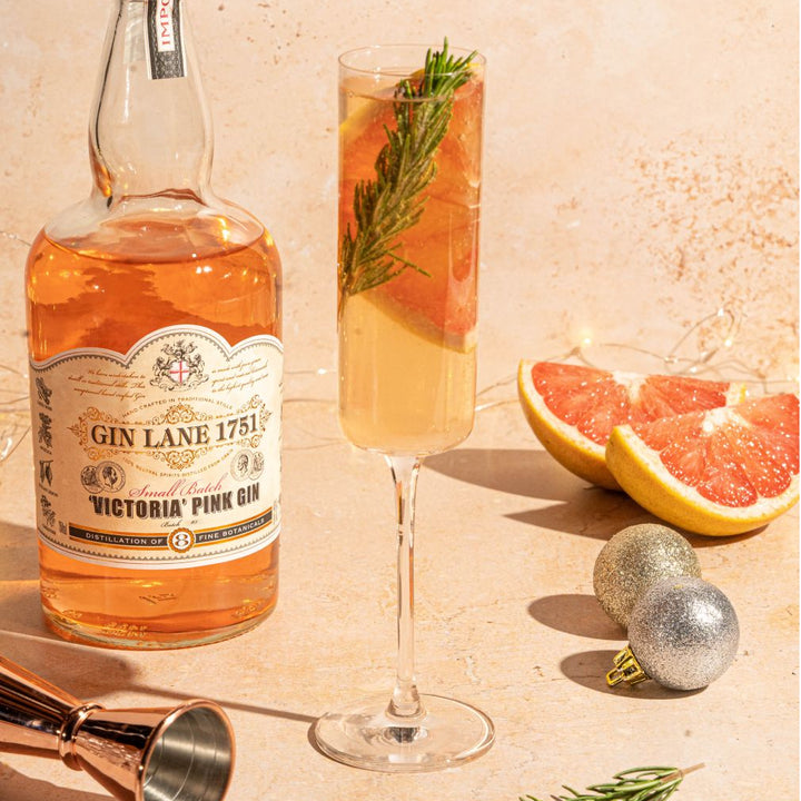 Bottle of Gin Lane 1751 Victoria Pink Gin with a cocktail glass and garnishes on a beige background