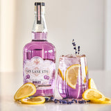 Purple bottle of Gin Lane 1751 Violet gin with a glass of lavender lemonade on a light background