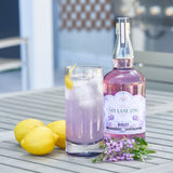Bottle of Gin Lane 1751 Violet gin with a glass of lemonade on a wooden surface.