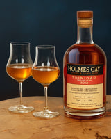Bottle of Holmes Cay Trinidad rum with two filled glasses on a wooden surface.