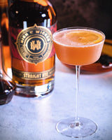 Cocktail in a glass with an orange slice next to a bottle of High West whiskey.