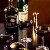 Bottles and glasses of coffee liqueur on a dark surface with a gold jigger.