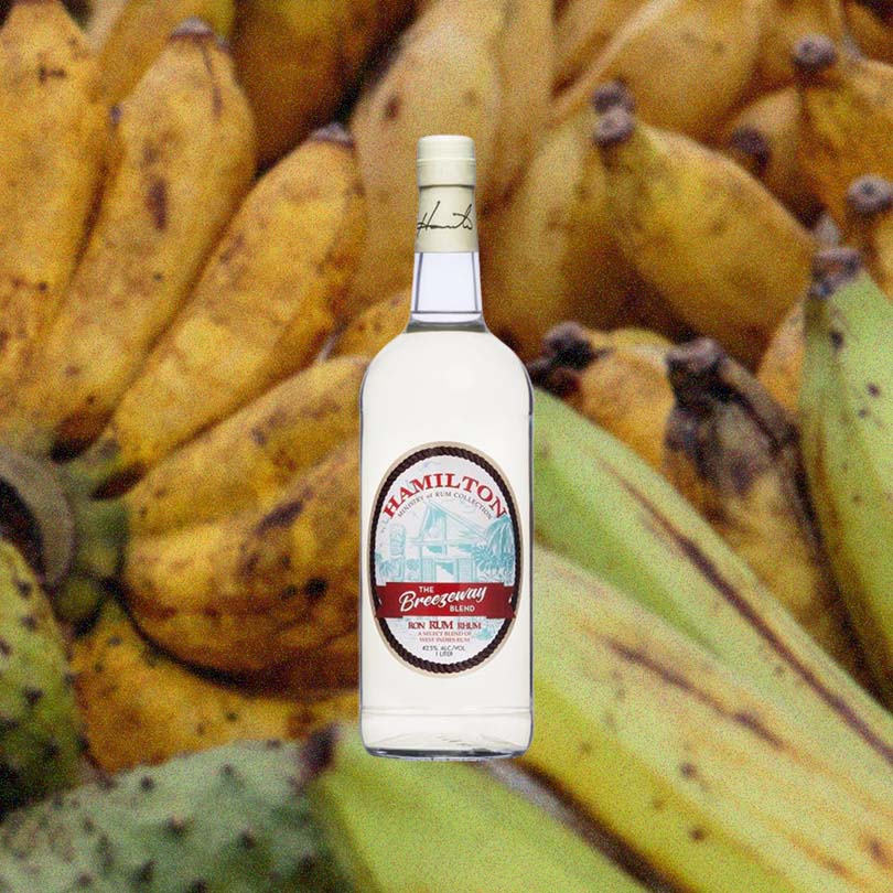 Bottle of Hamilton Breezeway Blend Rum over back drop image of bananas.