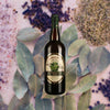 Bottle of Hamilton Pimento Dram Liqueur over backdrop image of purple flowers and spices.