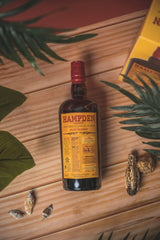 Hampden rum bottle on a wooden surface with leaves and a box in the background
