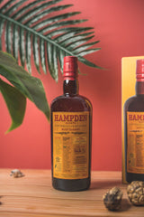 Hampden rum bottle with a red cap on a wooden surface against a red background