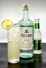 The Hawi Highball. A Collins glass with a light yellow liquid garnished with a lime wheel. In the middle a botle of Kuleana Rum Works. Just behind, a slightly out of focus bottle of Fever-Tree Lime & Yuzu soda water.