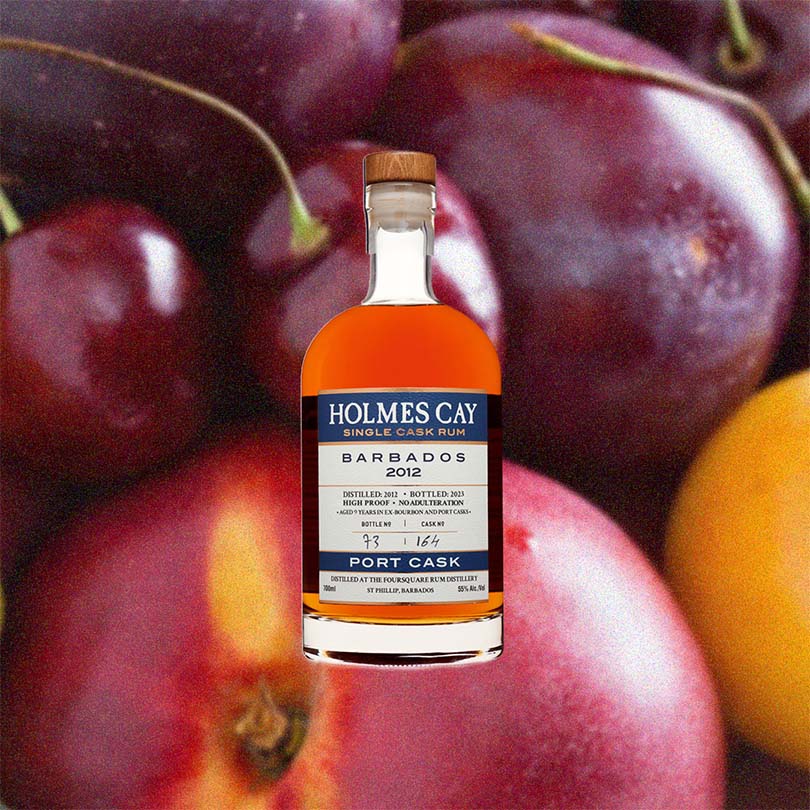 Bottle of Holmes Cay Barbados 2012 Port Cask Rum over back drop image of cherries.
