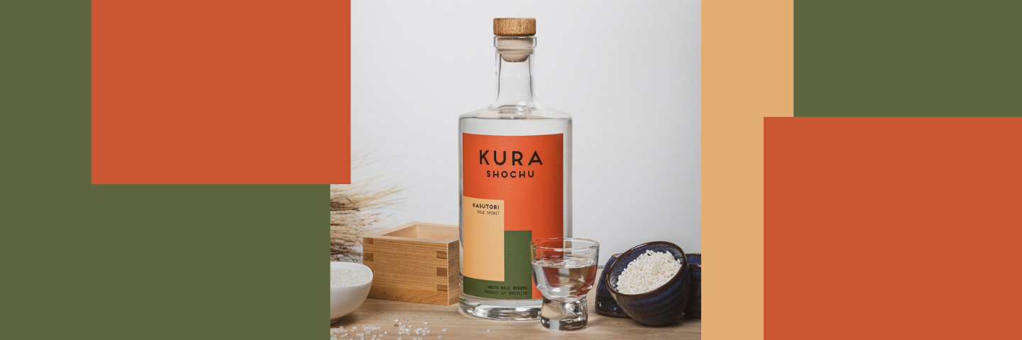 Kura Shochu bottle with a glass on a wooden surface with colorful geometric shapes.
